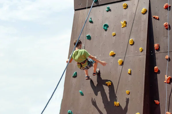 Młody wspinacz skalny schodzi ze sztucznej góry z bezpiecznymi linkami i sznurami w sportowym parku rozrywki. — Zdjęcie stockowe