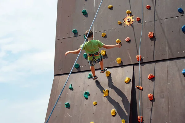 A young rock climber descends from an artificial mountain with safety cords and ropes in a sports amusement park. — Stock Photo, Image