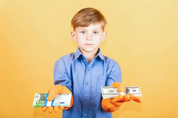 A child in a blue shirt and washing gloves is holding a pack of dollars in one hand and a pack of euro notes in the other. The concept of financial independence with clean hands.