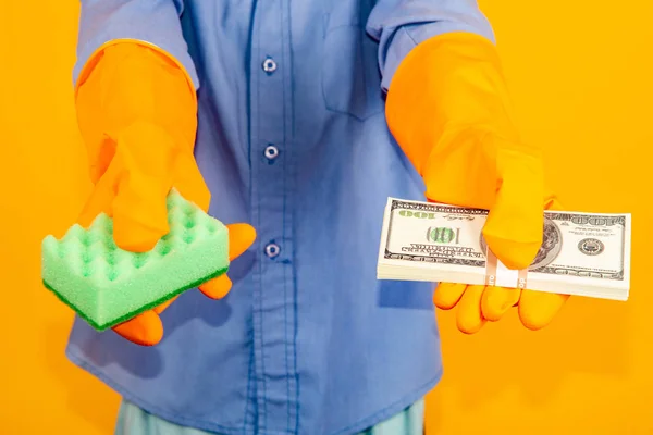 De jongen in het wassen van handschoenen houdt een pakje dollars in de ene hand en een spons in de andere. Het concept van het witwassen van geld en belastingontduiking. — Stockfoto