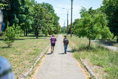 Bir kız ile bir çocuk arkasında ders kitapları ile sırt çantaları tutarak, okula parka gitmek.