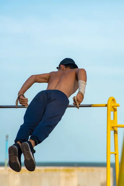 De jongen op de bar voert de oefeningen, een sterke en gespierde atleet. — Stockfoto