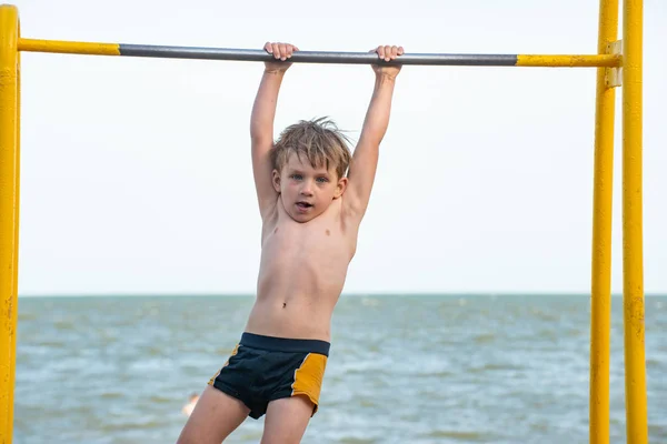 De jongen op de bar voert de oefeningen, een sterke en gespierde atleet. — Stockfoto