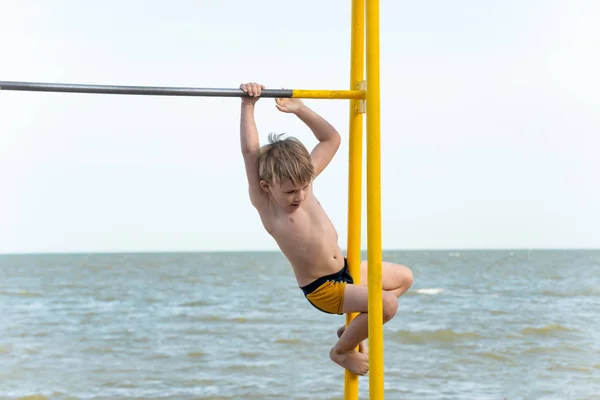 Mały sportowiec sportowy, chłopiec próbuje wspiąć się na poziome bar. — Zdjęcie stockowe
