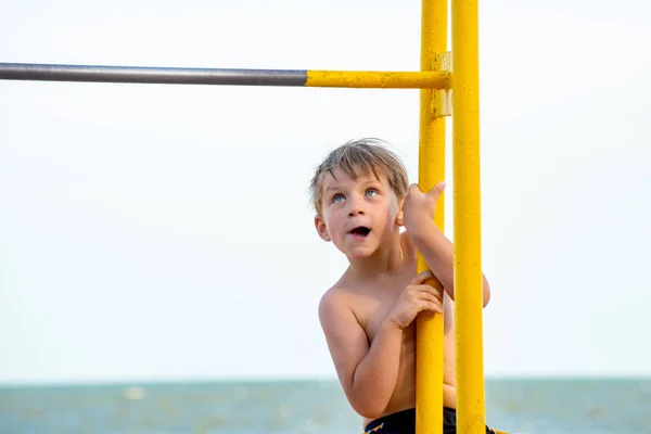 A little sports athlete, a boy is trying to climb the horizontal bar. — Stock Photo, Image
