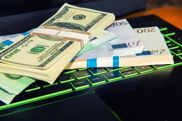 Money on a laptop, bundles of dollars and euros are on the keyboard of a laptop, the concept of online wages and the Internet win.