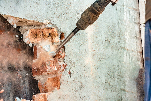 Disassembly of walls and openings with an electric jackhammer, close-up, dust hoarse from under the chisel.