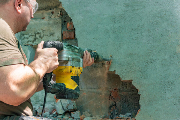 Dismantling walls and openings with an electric jackhammer. The worker in goggles performs repair work.
