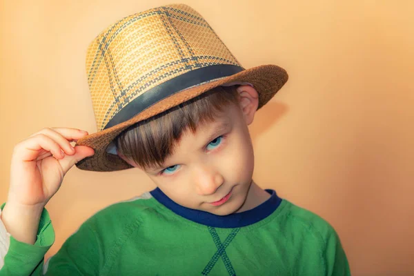 Um menino de chapéu de palha transmite uma saudação, um retrato de uma criança em um fundo bege. . — Fotografia de Stock