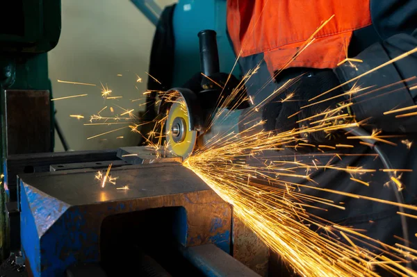 Een werknemer zaait een metalen blank met een snij wiel met een slijpmachine, grote vonken vliegen rond. — Stockfoto