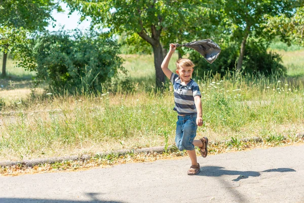 El niño corre por el parque y juega con una bolsa de celofán negro . —  Fotos de Stock