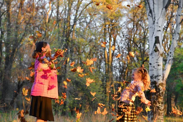 Щаслива мама і дочка кидають осіннє листя в парку, радісна сім'я . — стокове фото