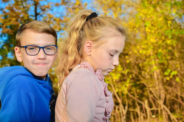 Ένα αγόρι με γυαλιά δίπλα σε ένα κορίτσι την πτώση στο πάρκο, μια νέα φιλία και στοργή. — Φωτογραφία Αρχείου