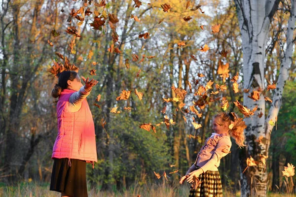 Feliz mamá y su hija arrojan hojas de otoño en el parque, familia alegre . —  Fotos de Stock