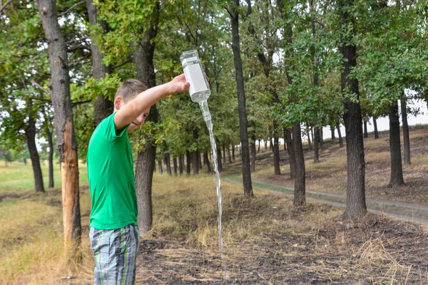 L'adolescent tient une bouteille d'alcool et verse de l'alcool au sol dans le parc. Problèmes d'alcoolisme infantile . — Photo