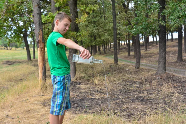 Genç bir şişe alkol tutar ve parkta yere likör döker. Çocuk alkolizmi sorunları. — Stok fotoğraf