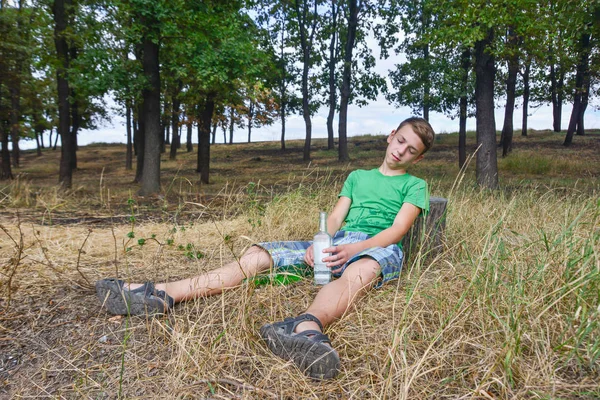 Ein Teenager mit Alkohol im Park, der Junge schläft nach einem Rausch. Probleme des Alkoholismus bei Kindern. — Stockfoto