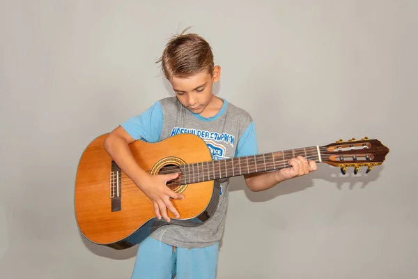 Un niño toca la guitarra sobre un fondo gris en el estudio, foto de primer plano de gran angular . —  Fotos de Stock