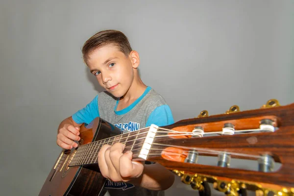 Un niño toca la guitarra sobre un fondo gris en el estudio, foto de primer plano de gran angular . —  Fotos de Stock