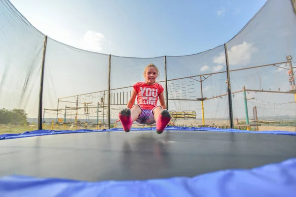 Een meisje in rode kleren springen op een trampoline in een pretpark. — Stockfoto