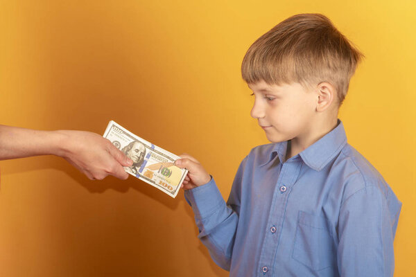 Мальчик в синей рубашке протягивает руку и берет доллары
.