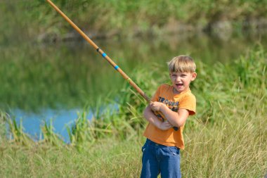 Nehirde bir balıkçı çocuk bir olta tutar, bir çocuk bir balık yakaladı ve bir kanca üzerinde sudan çıkarır.