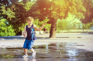Çocuk yağmurda koşar, parkta güneşli bir gün.
