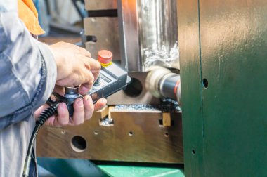 İşçi, ürünün öğütülmesi ve imalatı için bir cnc makinesinde uzaktan kumandayı kontrol eder.