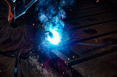 Kaynakçı metal ürünlerden metal yapılar yapar ve bir kaynak ile bağlanır.