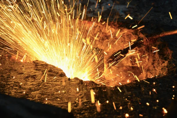 Een gassnijder in productie, een lasser verwijdert onnodige metaalresten met een gassnijder, vonken vliegen in verschillende richtingen. — Stockfoto