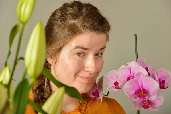 Ein schönes Mädchen mit einer Orchidee in der Hand genießt den Duft von Blumen und posiert im Studio für die Kamera. — Stockfoto