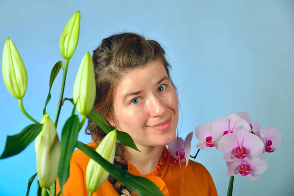 Ein schönes Mädchen mit einer Orchidee in der Hand genießt den Duft von Blumen und posiert im Studio für die Kamera. — Stockfoto