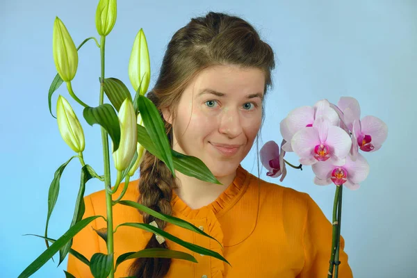 Egy gyönyörű lány, egy orchidea a kezében élvezi a virágok illata és pózok a kamera a stúdióban. — Stock Fotó