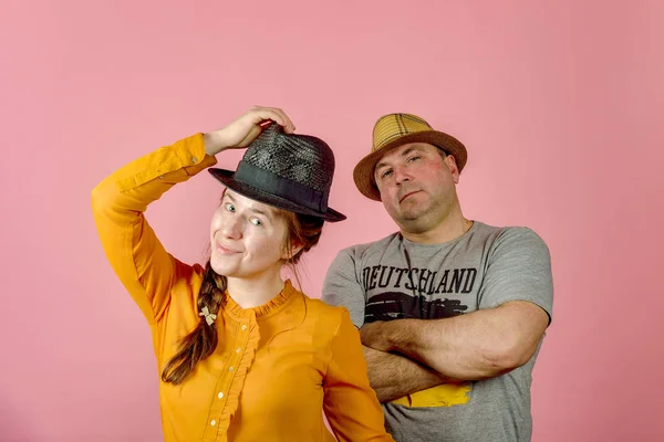 Kırmızı arka plan üzerinde hasır şapkalı bir adam ve bir kadın stüdyoda kameraya poz verirken. — Stok fotoğraf