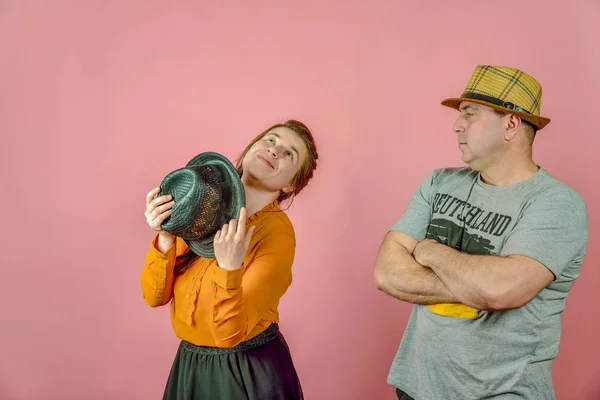 Kırmızı arka plan üzerinde hasır şapkalı bir adam ve bir kadın stüdyoda kameraya poz verirken. — Stok fotoğraf