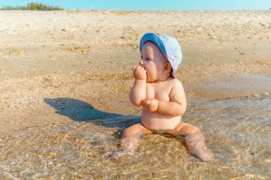 Deniz kıyısında küçük bir çocuk deniz suyunda kum yiyor.