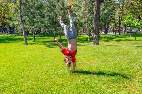 Um rapaz está de pernas para o ar num parque na relva verde. . — Fotografia de Stock