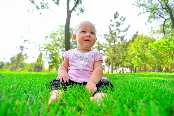 A joyful and happy little girl sits on the green grass and looks around. — Stock Photo, Image