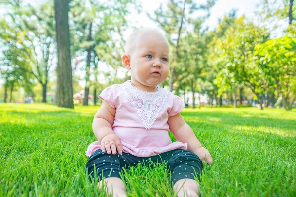 A joyful and happy little girl sits on the green grass and looks around. — Stock Photo, Image