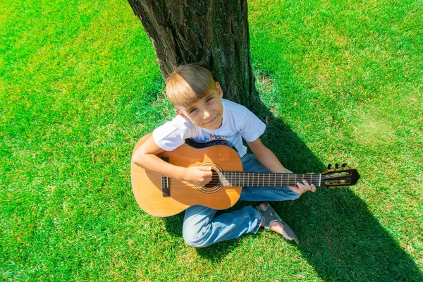 Barnet spelar gitarren i naturen, uppifrån. — Stockfoto