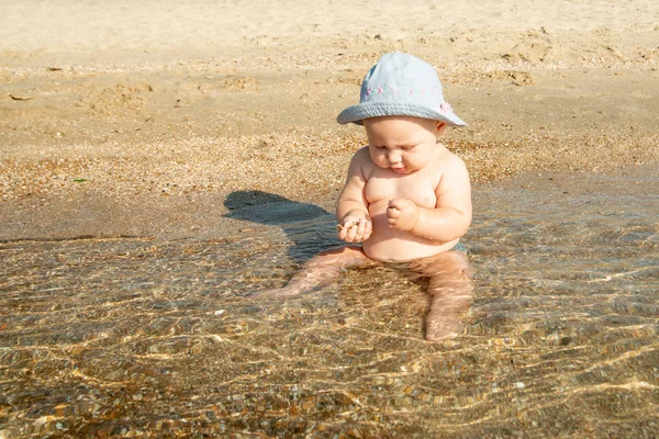 Małe dziecko na brzegu morza zjada piasek w wodzie morskiej. — Zdjęcie stockowe