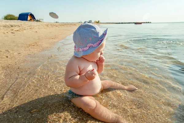 Un bambino piccolo sulla riva del mare mangia sabbia in acqua di mare . — Foto Stock
