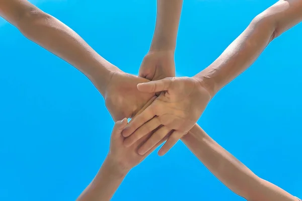 Friends hold hands together, bottom view of a group of people clasped hands.