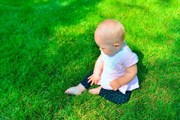 Little girl sitting on the green grass, top view. — Stock Photo, Image
