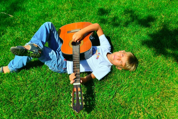 Un joven músico está tumbado en la hierba verde con una guitarra en sus manos, vista superior . —  Fotos de Stock
