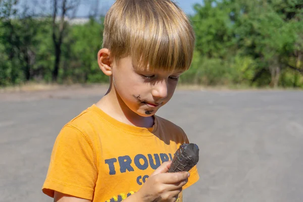 Gelato nero nelle mani di un bambino, il ragazzo mangia gelato nero, viso e bocca sporchi . — Foto Stock