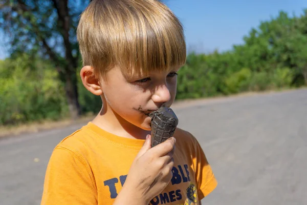 Schwarzes Eis in den Händen eines Kindes, der Junge isst schwarzes Eis, verschmutztes Gesicht und Mund. — Stockfoto