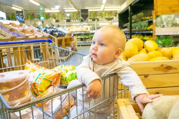 Un niño en un supermercado en un carro vigila las compras de los padres . — Foto de Stock