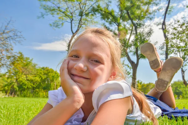 A young and beautiful girl lies on the green grass in the park and looks at the camera. — Stock Photo, Image