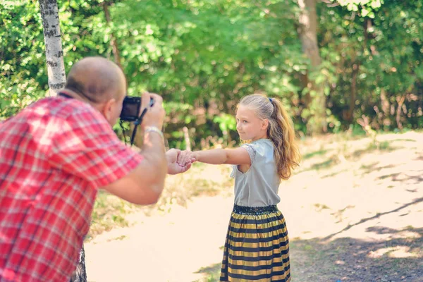 Um homem fotografa uma menina caminhando pela floresta . — Fotografia de Stock